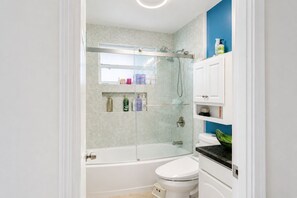 A bathroom with a glass-enclosed shower, a white toilet, and shelves with toiletries. - Serene Amenity filled 1-bedroom in host-shared home in charming Fullerton (Fullerton)