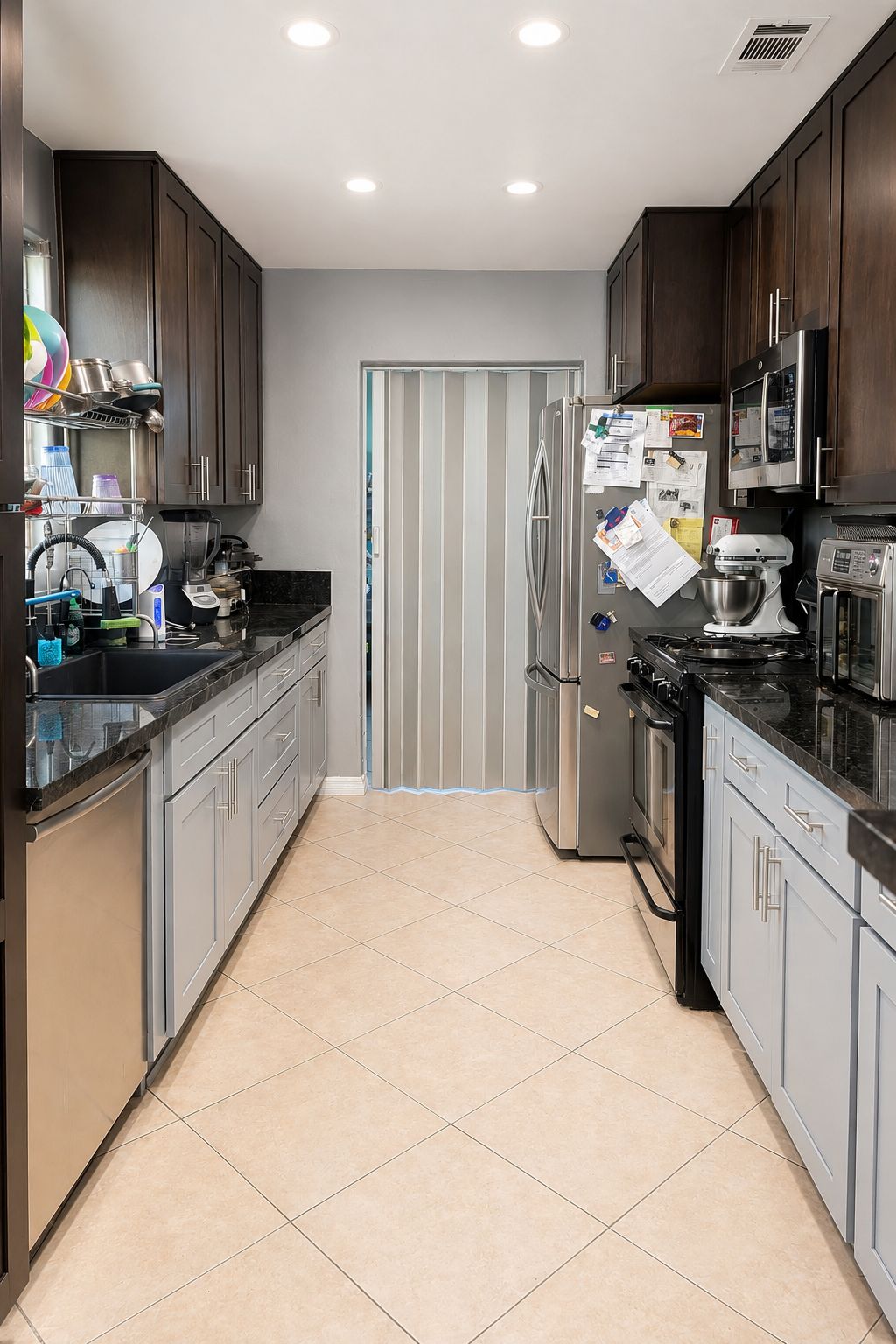 A modern kitchen with stainless steel appliances, grey cabinetry, and a tiled floor.