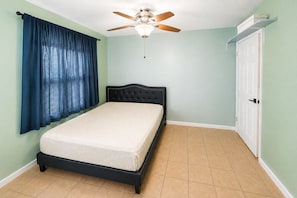 A bedroom with a bed, a ceiling fan, a window with curtains, and a door. - Serene Amenity filled 1-bedroom in host-shared home in charming Fullerton (Fullerton)