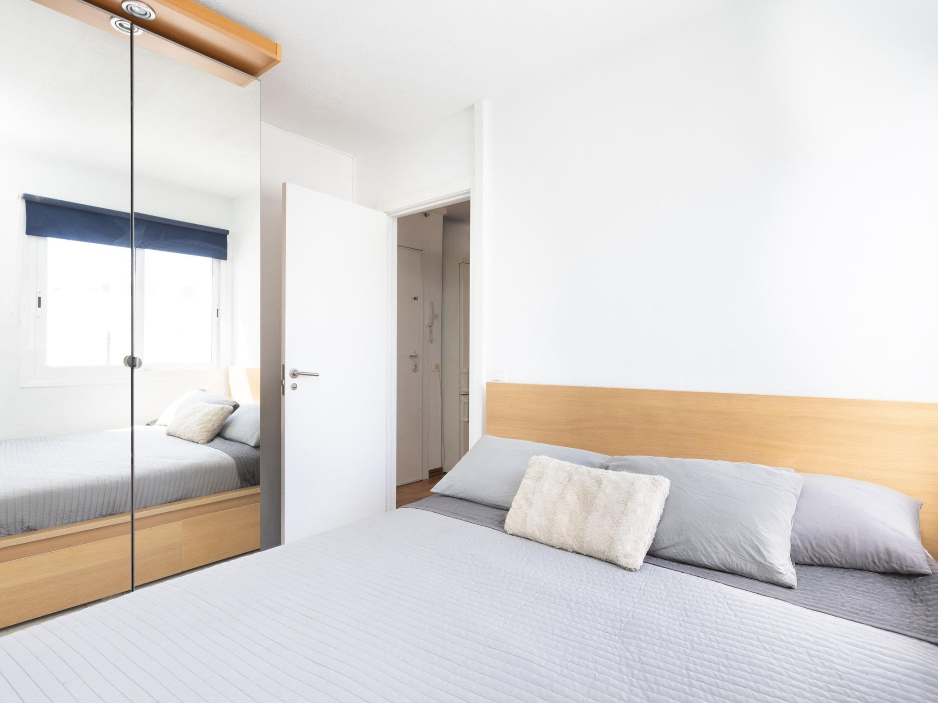 Ein Schlafzimmer mit einem großen Bett, einem Schrank mit Spiegel und einer Tür zu einem weiteren Raum.