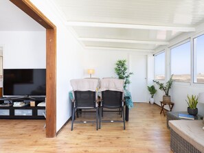 Ein Wohnzimmer mit Fernseher, zwei Sesseln, einem Tisch und Blick ins Freie.