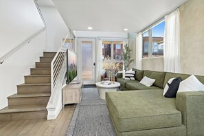 A modern living room with a staircase, a green sofa, and a view of the city through a glass door. - Queen Anne~Walk to Space Needle~City/Sound Views (Seattle)