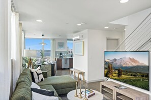 Ein modernes Wohnzimmer mit einem grünen Sofa, einem Couchtisch und einem Flachbildfernseher, der eine Berglandschaft zeigt.