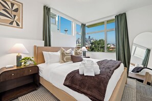 A hotel room with a bed, a nightstand, a lamp, a plant, and a view of the cityscape. - Queen Anne~Walk to Space Needle~City/Sound Views (Seattle)