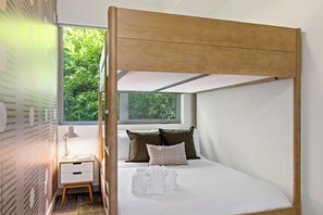 Ein modernes Schlafzimmer mit einem hölzernen Baldachinbett, einem Nachttisch mit Lampe und Blick auf Grünflächen.