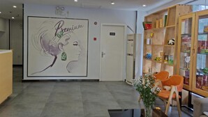 Zona de recepción con un mural grande en la pared, mostrador de recepción, vitrina de madera y un área de descanso con sillas.
