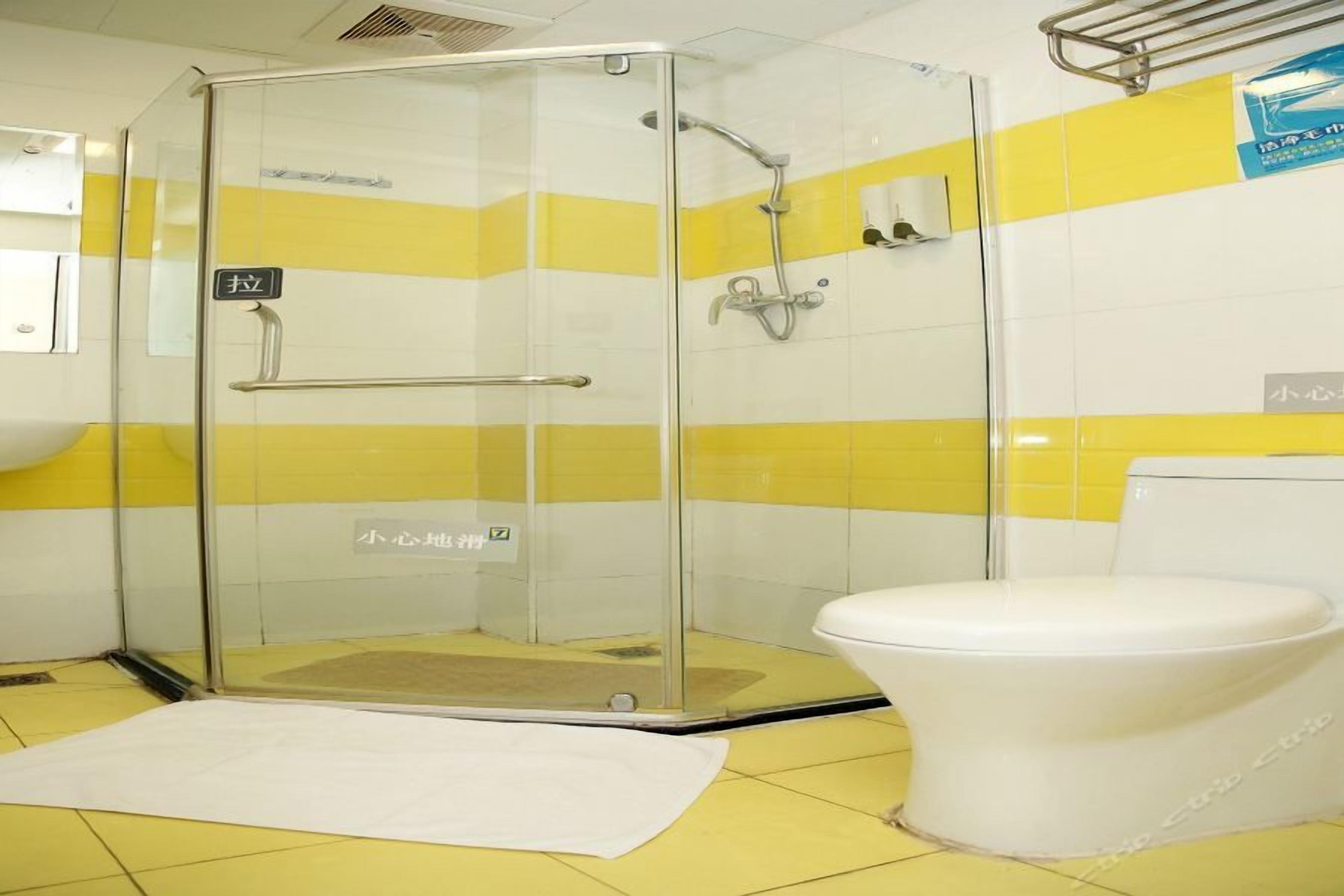A bathroom with a glass-enclosed shower, a white toilet, and yellow and white tiled walls.