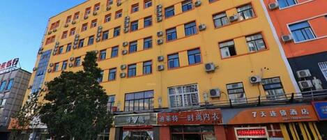 A multi-story building with a yellow facade, multiple windows, and air conditioning units.