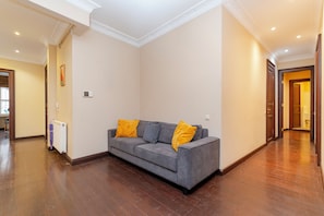 A modern living room with a grey sofa, two yellow cushions, a radiator, and a wooden floor. - Spacious 3BR, 2-Bath Ground-Floor Apartment in Central Istanbul (İstanbul)