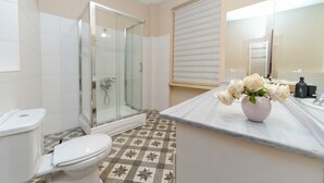 A bathroom with a glass shower enclosure, a toilet, a patterned floor, and a vanity with a vase of flowers. - Spacious 3BR, 2-Bath Ground-Floor Apartment in Central Istanbul (İstanbul)