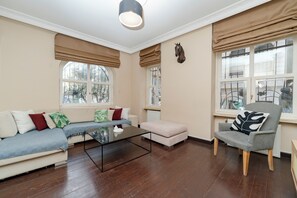 A living room with a sofa, ottoman, and armchair, a glass coffee table, and large windows with blinds. - Spacious 3BR, 2-Bath Ground-Floor Apartment in Central Istanbul (İstanbul)