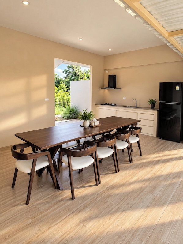 A modern kitchen with a dining area, wooden flooring, and a view of greenery outside.