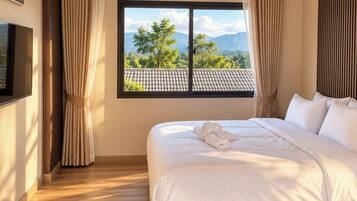 Habitación de hotel con una cama grande, televisión, ventana con cortinas y vistas a montañas.