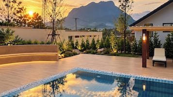 Una piscina con vista a la montaña, rodeada por un jardín paisajístico y un edificio moderno.