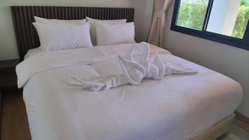 Habitación de hotel con una cama grande, cabecera, ventana con cortinas y vistas al exterior con vegetación.
