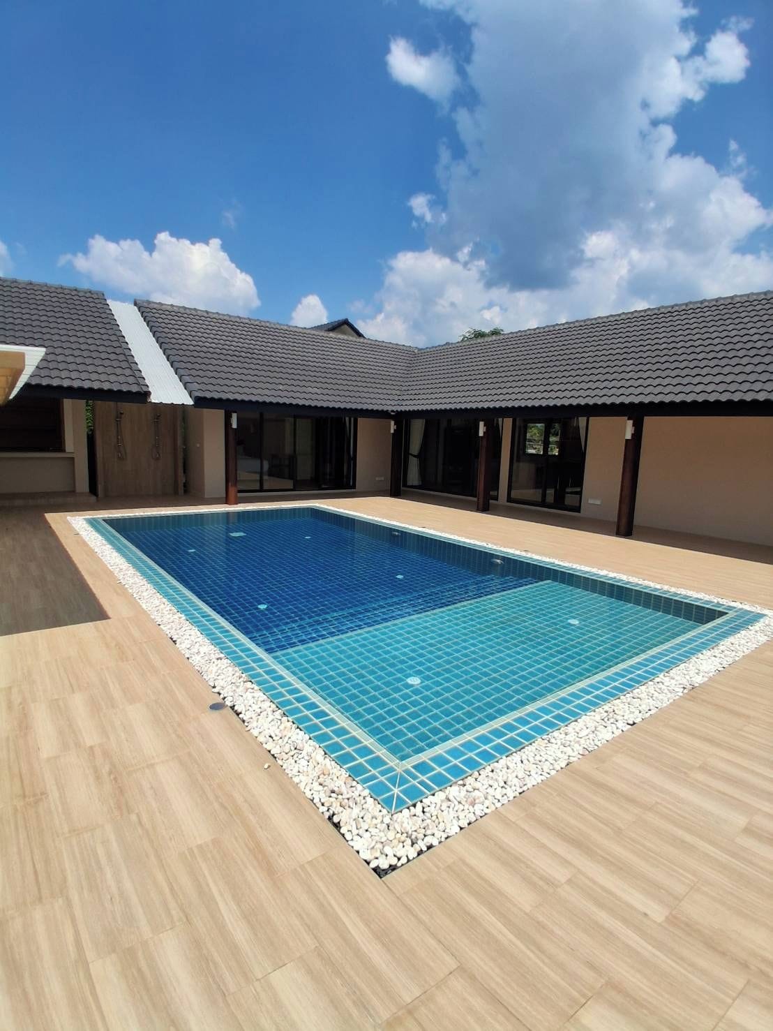 Una piscina rectangular con borde de azulejos, rodeada por un muelle de madera y una cuneta de grava.