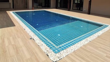 Una piscina rectangular con borde de azulejos, rodeada por un muelle de madera y una cuneta de grava.