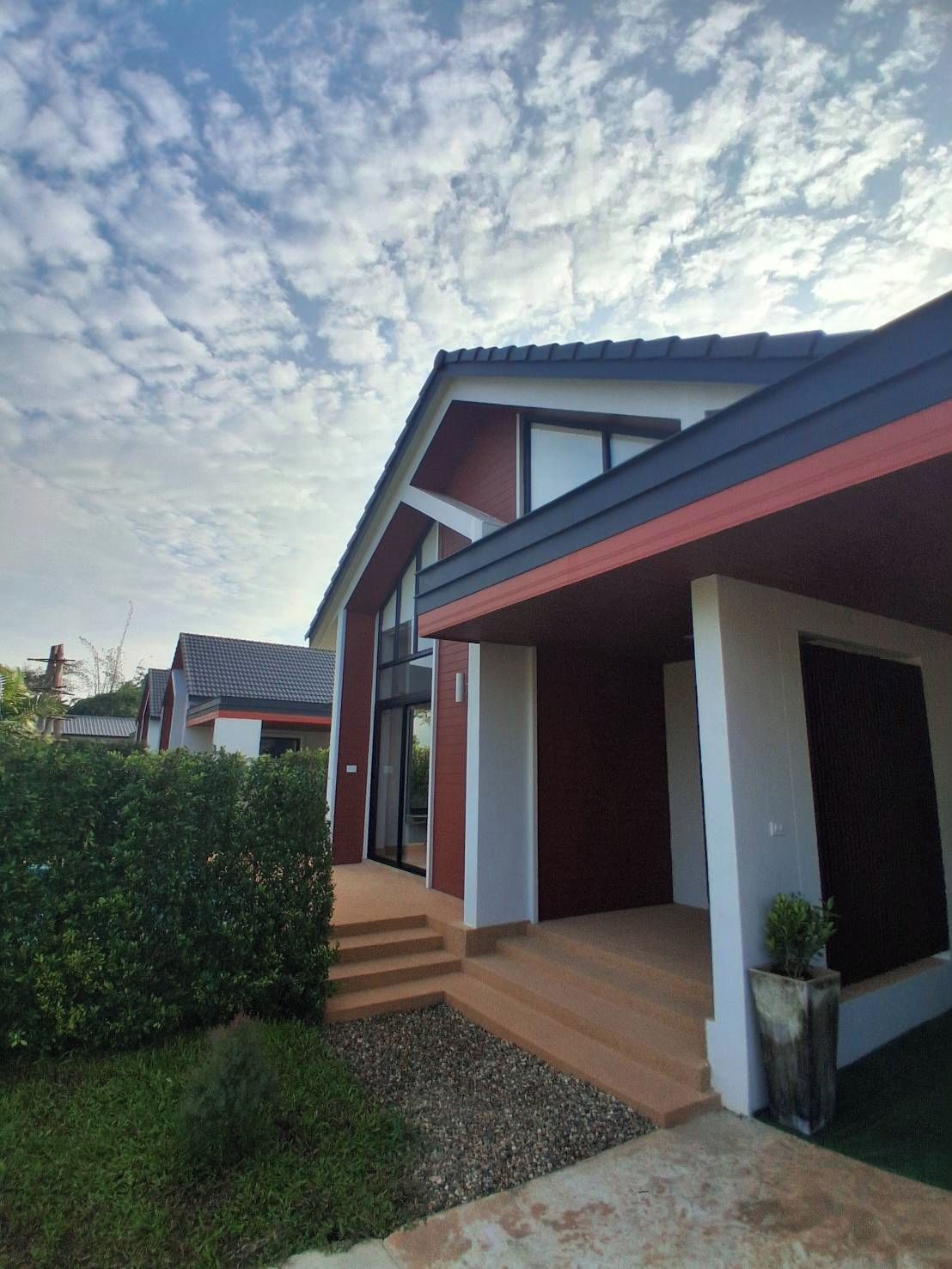Una casa moderna con fachada roja y blanca, un porche cubierto y un jardín cuidado.