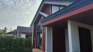 Una casa moderna con fachada roja y blanca, un porche cubierto y un jardín cuidado.