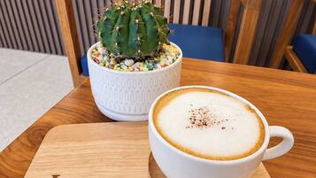 Una mesa de madera con una taza blanca de café y un cactus en una maceta blanca.