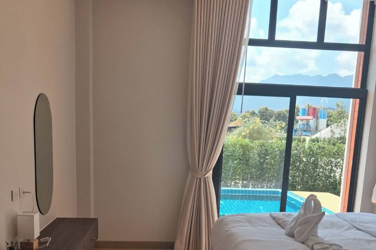 Habitación de hotel moderna con una cama grande, un aparador de madera, un espejo y vistas a una piscina.