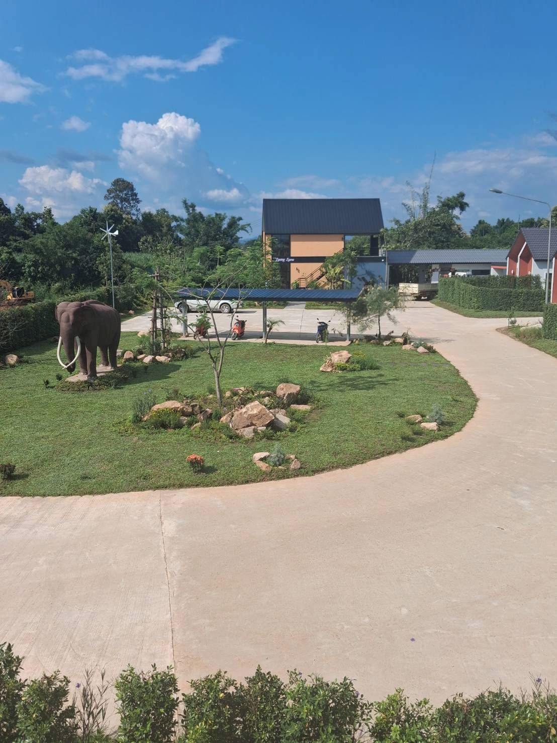 A pathway leading to a building with a wind turbine, an elephant, and a small tree.