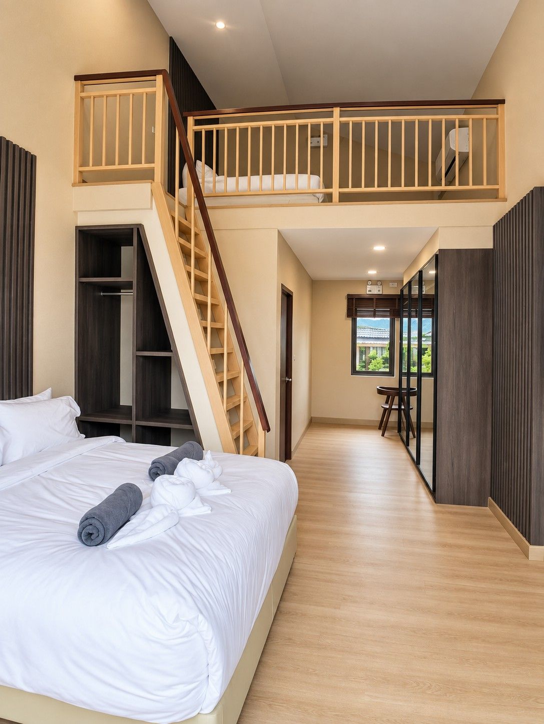 Un dormitorio con una cama grande, una escalera de madera, un armario empotrado y vistas a través de un ventanal.