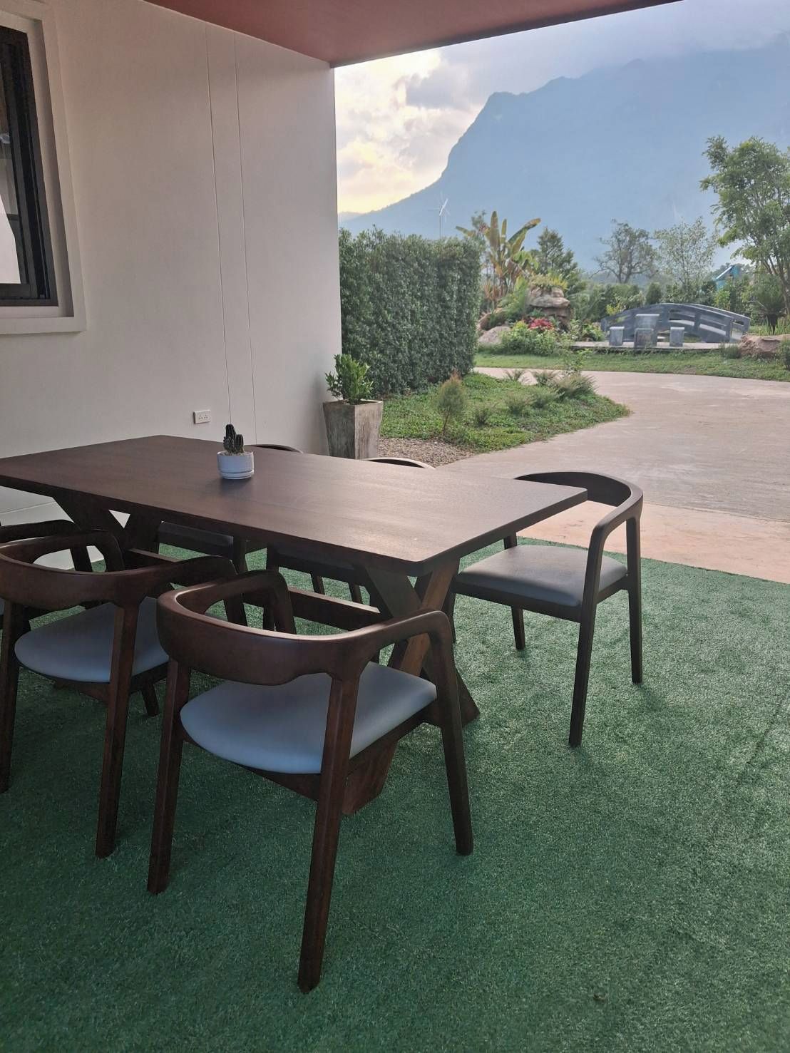 Un patio exterior con mesa y sillas de madera, una planta en maceta y vistas a la montaña.