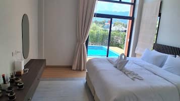 A hotel room with a large bed, a bedside table with a mirror, a small potted plant arrangement, a view of a pool and mountains through the window.