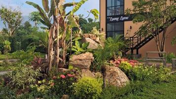 A building with a sign reading 'Luang Lum' surrounded by a landscaped garden with rocks, plants, and a banana tree.