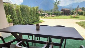 A dining table with chairs and a small bowl on it, set on artificial grass with a mountain view in the background. - Luang Lume Pool (Chiang Dao)