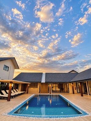 Una piscina con un deck de baldosas, un patio cubierto y un edificio con techo de tejas.