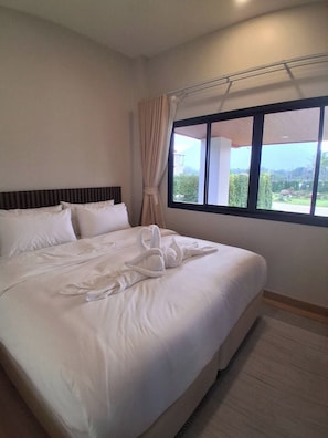 A hotel room with a large bed, a window with a view, and a curtain.