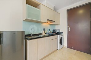 A compact kitchen with a stainless steel refrigerator, a built-in microwave, and a washing machine. - Sena by Kozystay - Menteng (Central Jakarta)