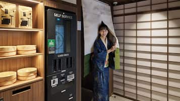 A self-service card deck with cash, credit card, and change options, and a woman in traditional attire standing beside it.