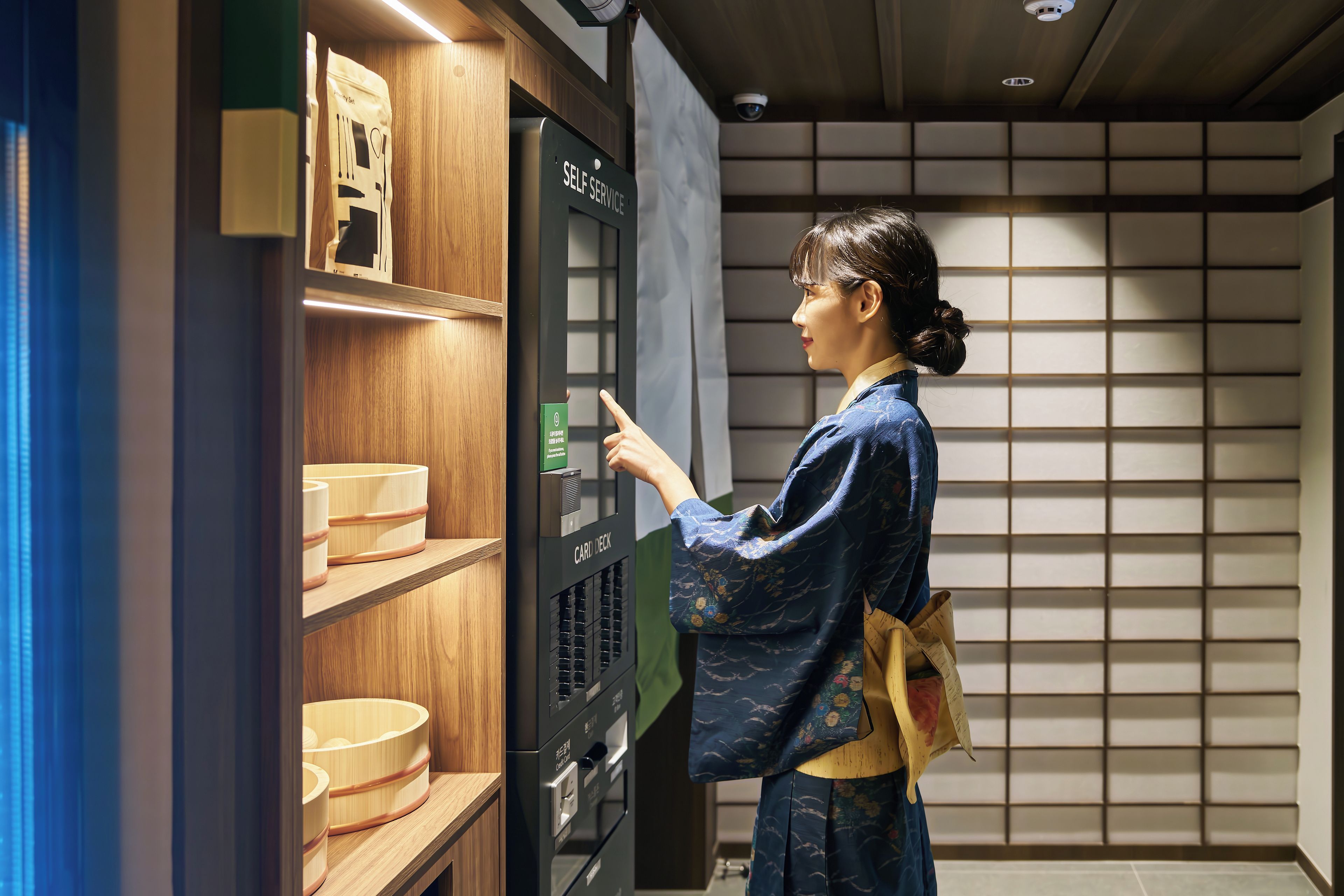 A person interacting with a self-service kiosk in a room with wooden shelves and a traditional Japanese sliding door.
