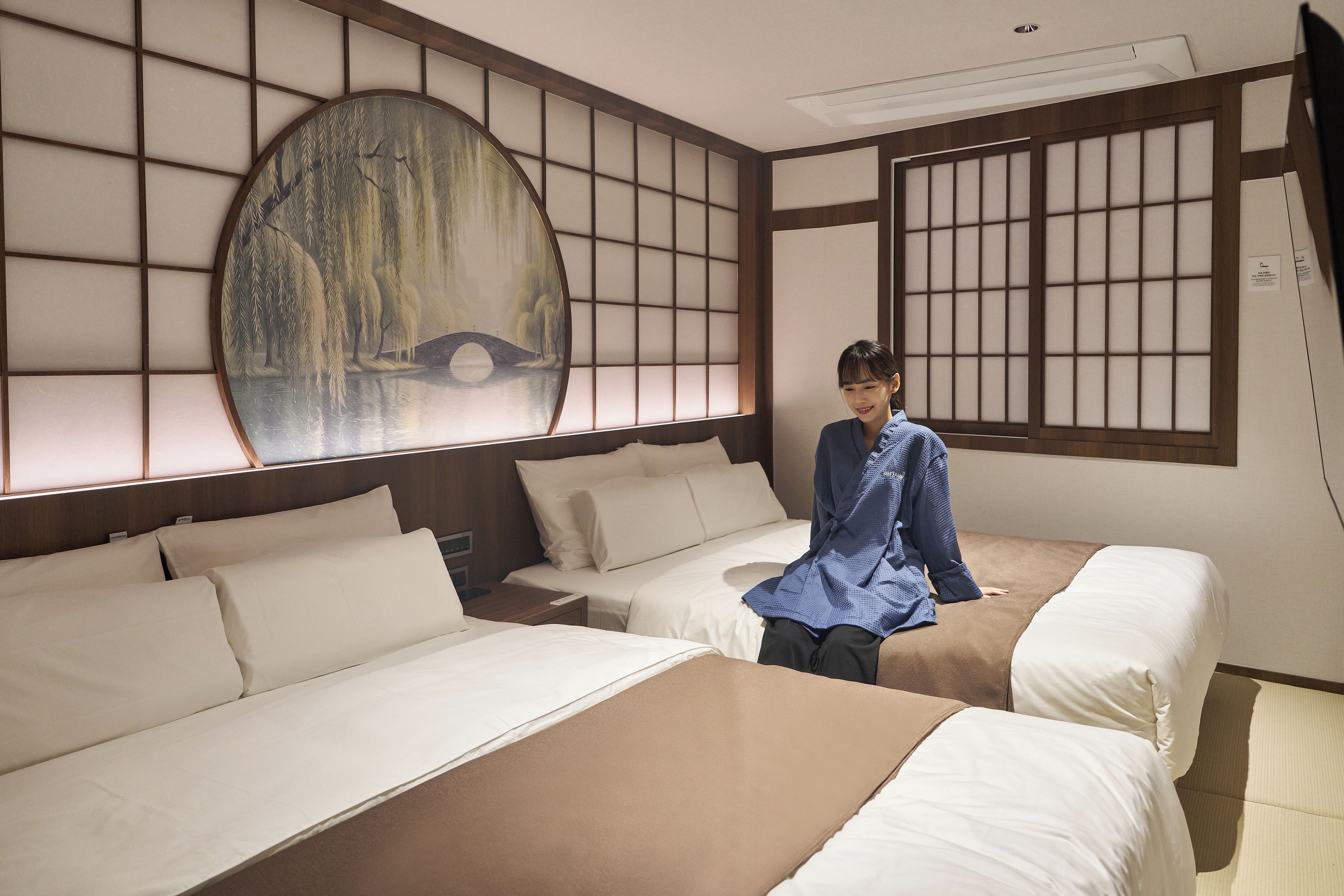 Une chambre d’hôtel avec deux lits, un grand tableau représentant un pont et une fenêtre de style japonais traditionnel.