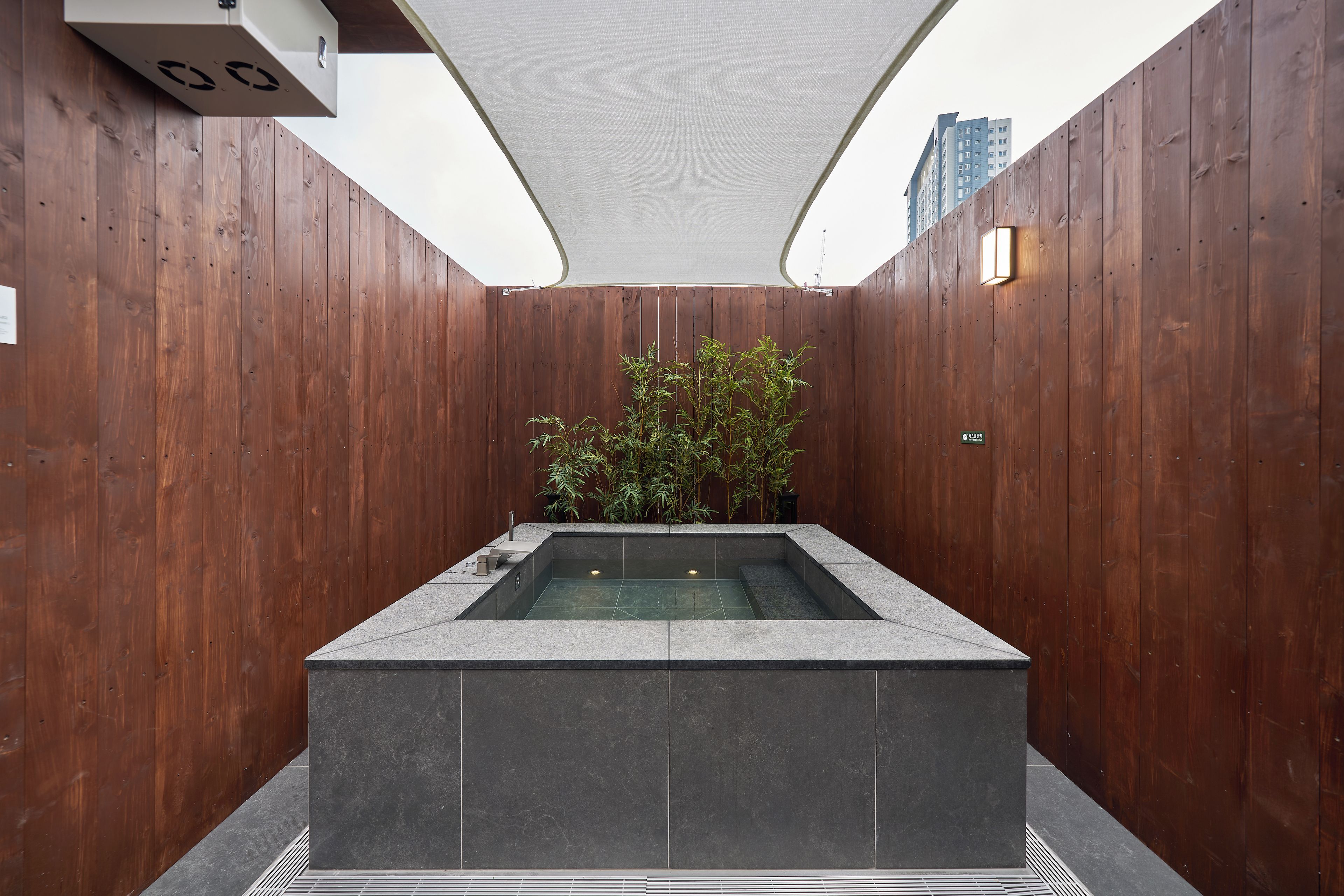 A spa area with a rectangular hot tub, wooden walls, and a bamboo plant.