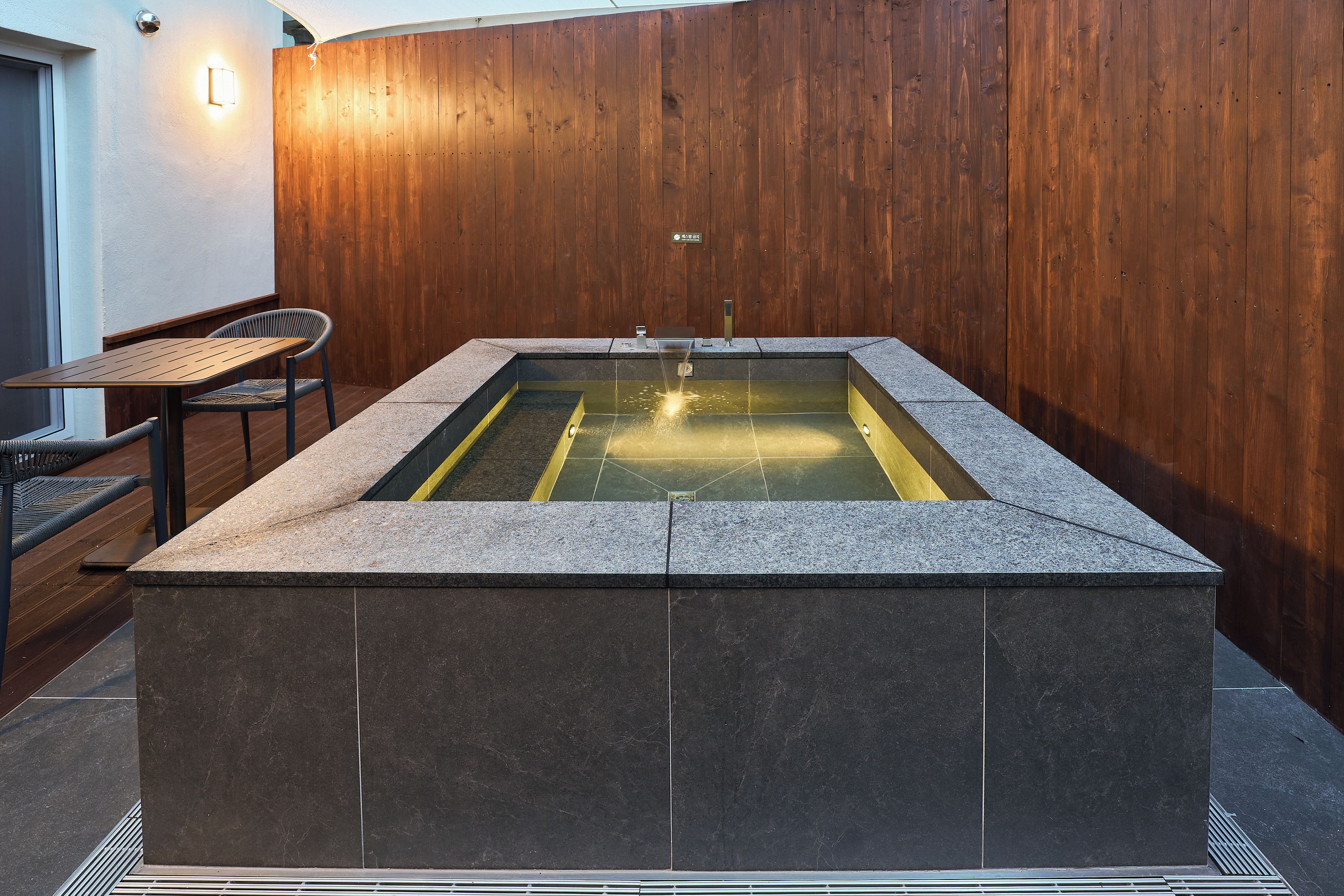A spa area with a stone hot tub, wooden wall, and seating.