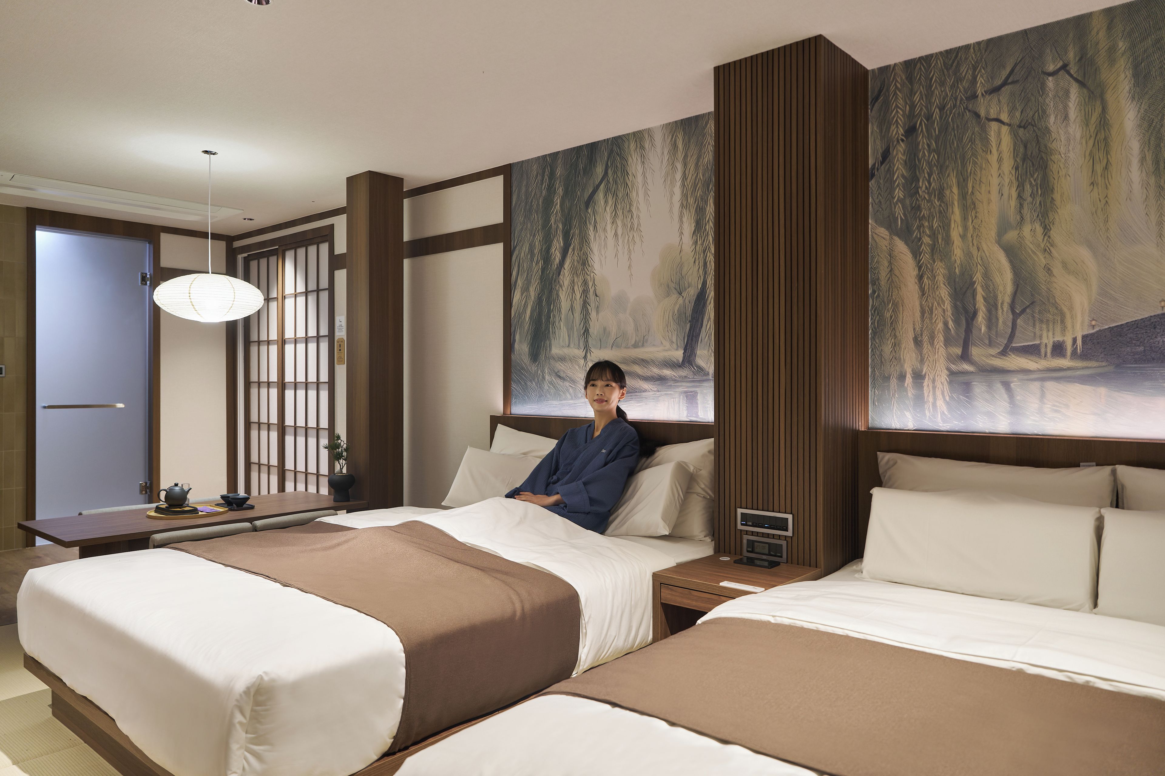 Una habitación de hotel con una cama grande, mesitas de noche, un escritorio y un cuadro de un paisaje boscoso.