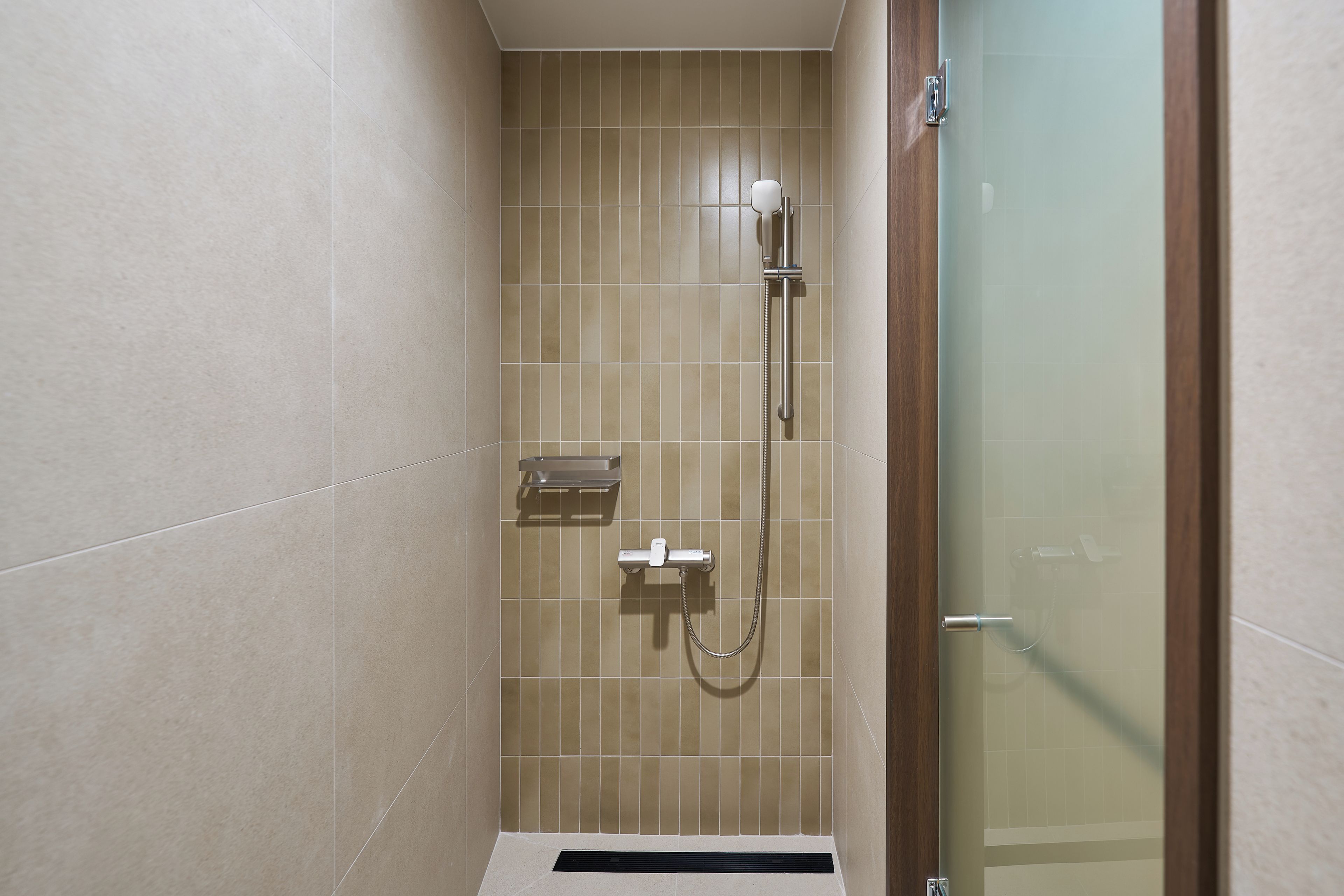 A small, modern shower area with a glass door, a handheld showerhead, and a wall-mounted faucet.