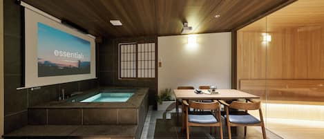 A modern interior with a wooden ceiling, a large screen displaying 'essential', a hot tub, and a dining area with chairs and a table.