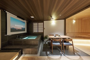 Un interior moderno con techo de madera, una pantalla grande mostrando 'essential', un jacuzzi y un comedor con sillas y mesa.
