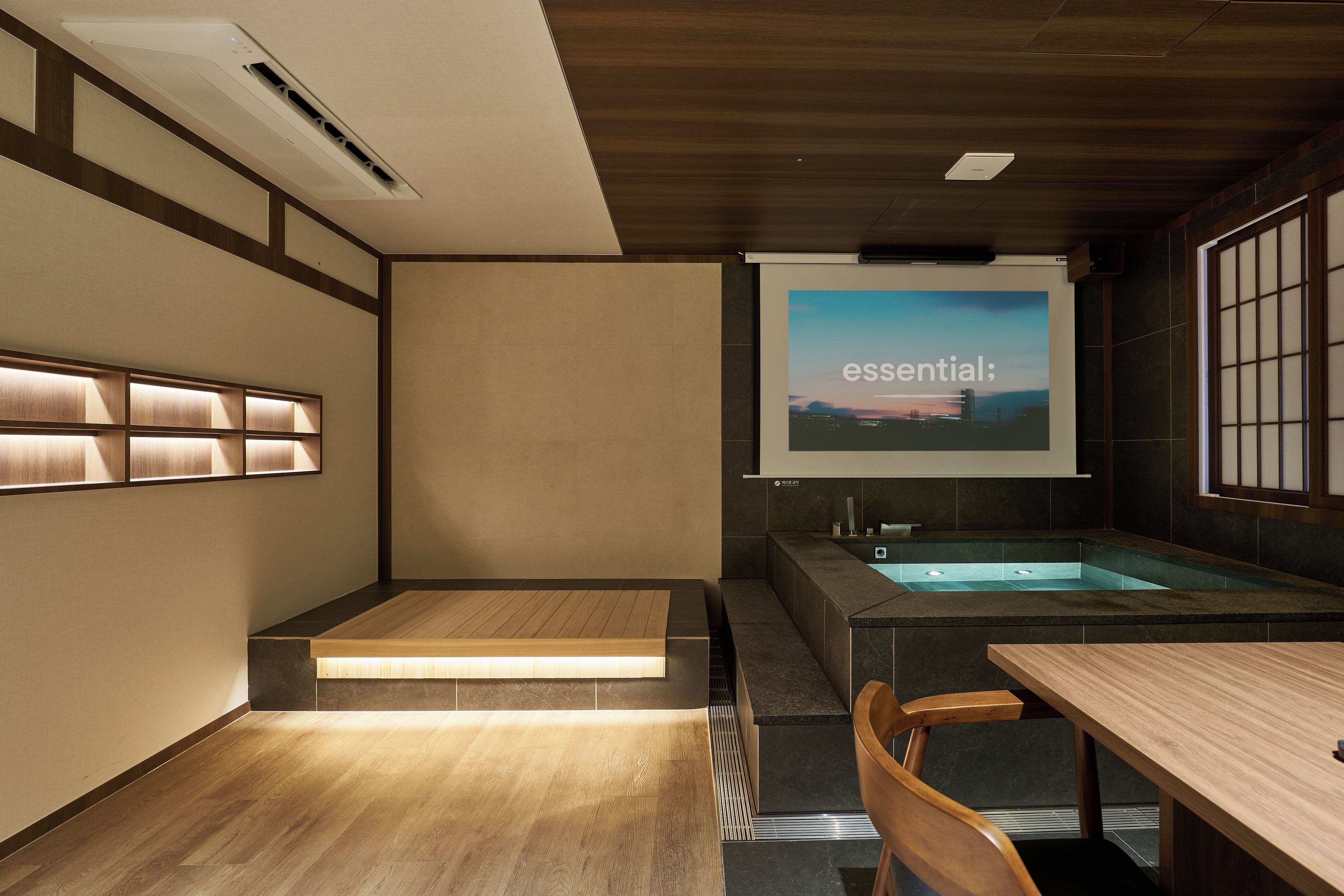 Un baño moderno con suelo de madera, una bañera, un lavabo y una pantalla de proyección que muestra la palabra 'essential'.