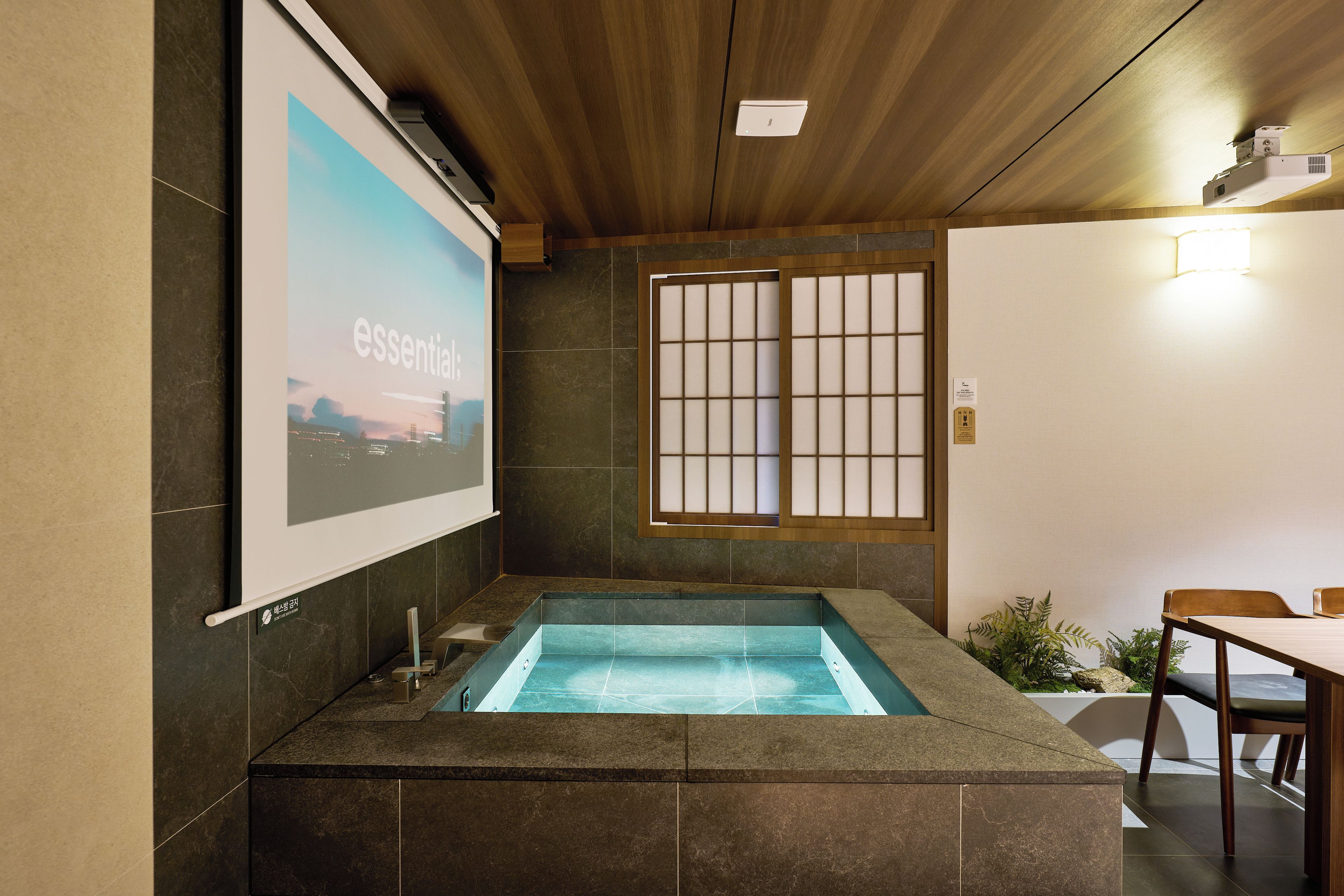 Una habitación con una piscina pequeña, una pantalla de proyector mostrando la palabra 'essential' y un tradicional puertas correderas japonesas.