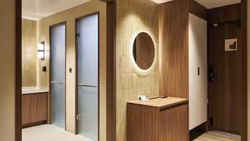 A hotel bathroom with a wooden vanity, a mirror, and a tiled wall.