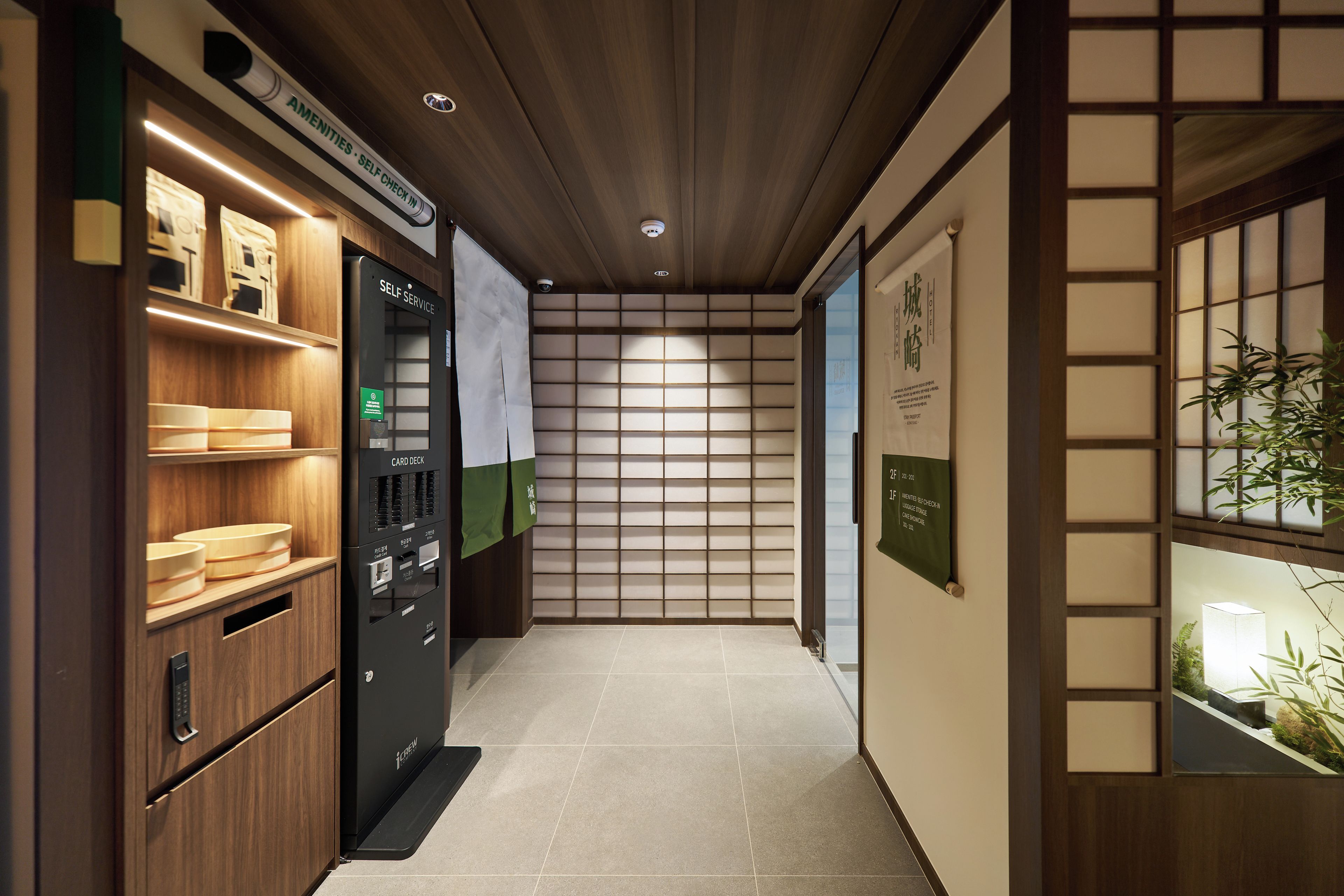 A hotel corridor with a self-service card machine, wooden shelves, and a traditional Japanese sliding door.