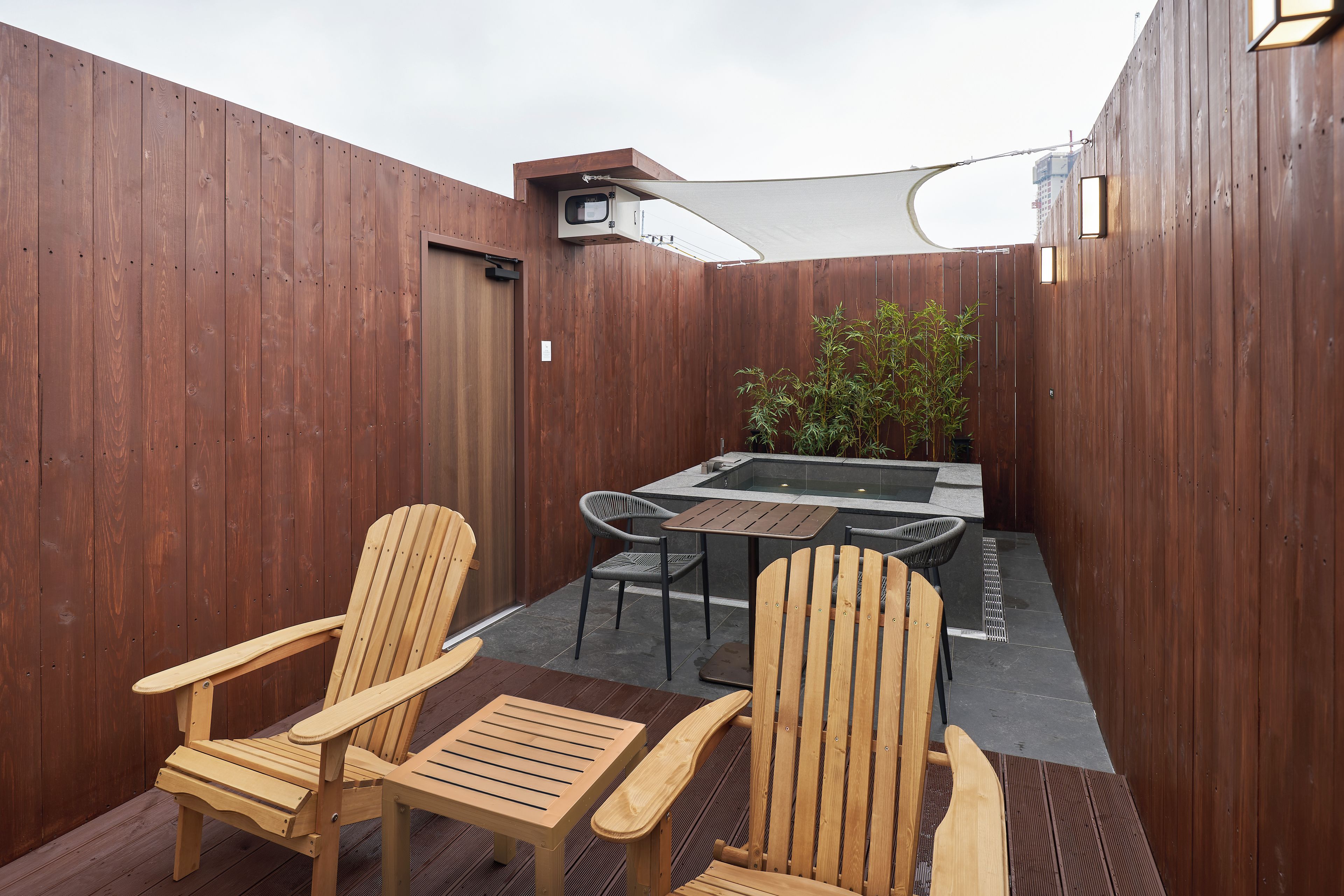 Un patio exterior con sillas de madera, una mesa y un jacuzzi.