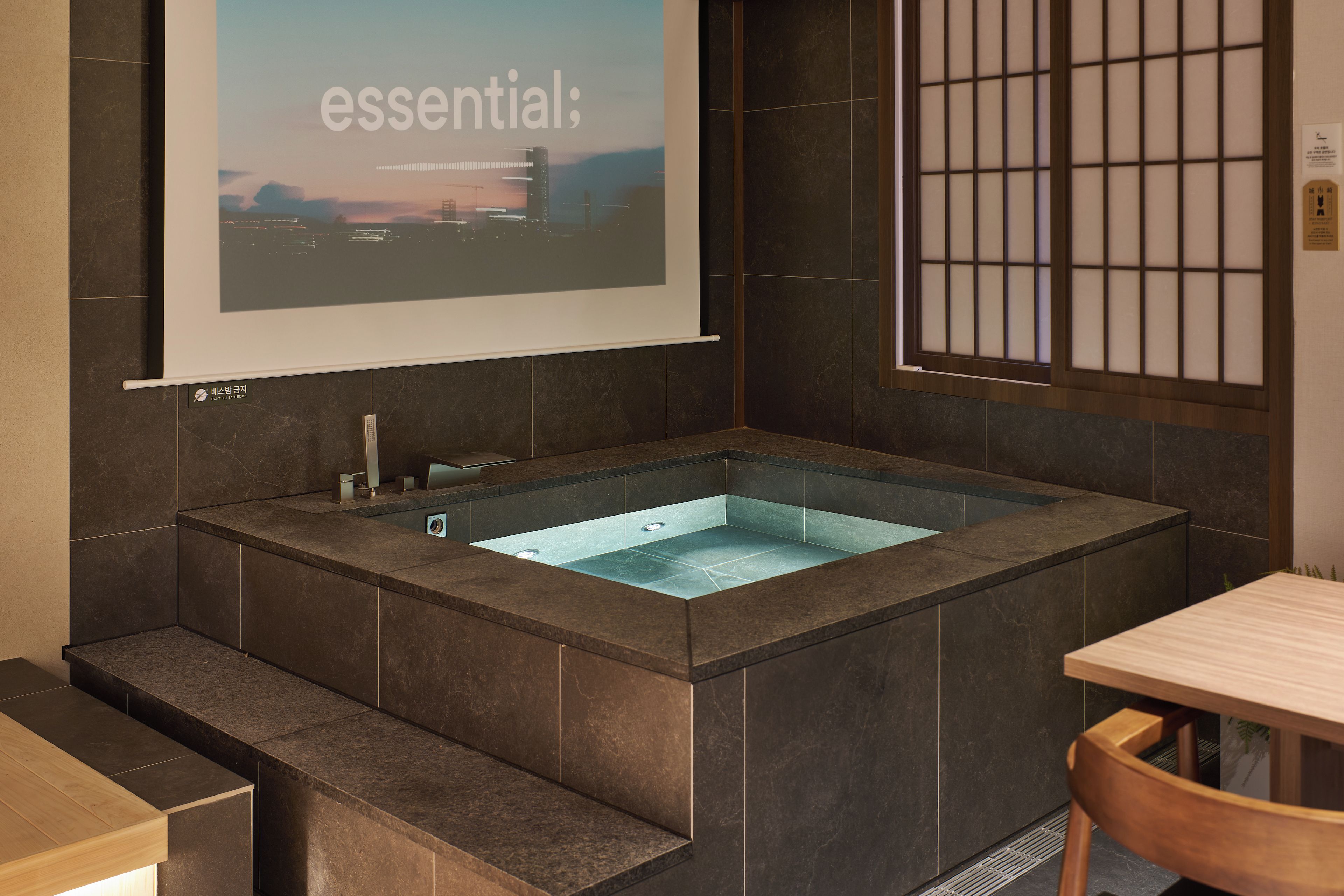 A modern bathroom with a large bathtub, a shower area, and a projection screen displaying the word 'essential'.