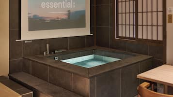 A modern bathroom with a large bathtub, a shower area, and a projection screen displaying the word 'essential'.